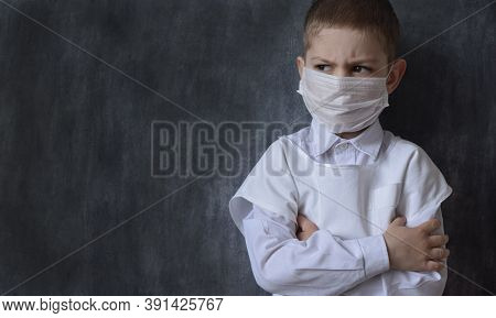 A Serious, Focused Boy In A Medical Mask And A White Coat, Stands Against The Background Of A Black 