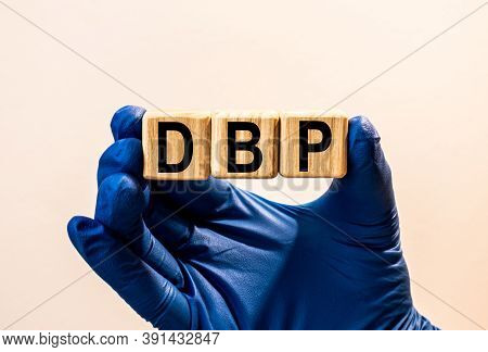 The Word Dbp Which Is Made From Wooden Cubes. Hands In A Blue Glove. Isolated On White Background.