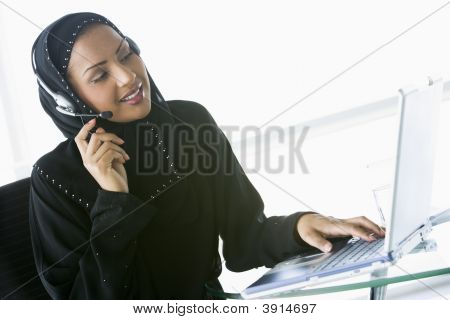 Middle Eastern Business Woman At Desk Using Laptop And Headset