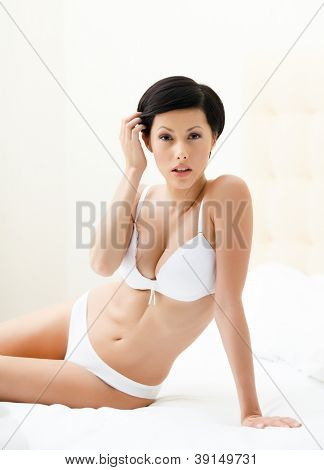Halfnaked kvinde sidder på den komfortable seng, isoleret på hvid baggrund
