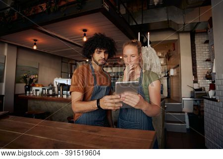 Young Serious Co-workers Using Digital Tablet While Standing In Modern Cafe