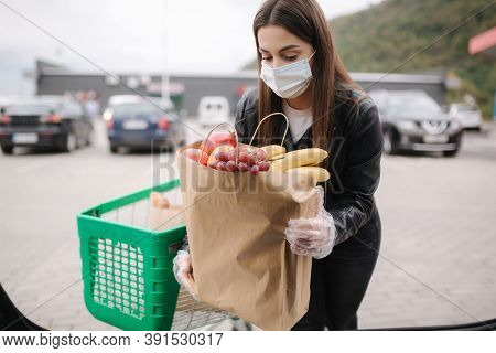 Over Trunk View Of Young Woman In Medical Mask In Masks Loading Bags In Trunk After Supermarket Shop