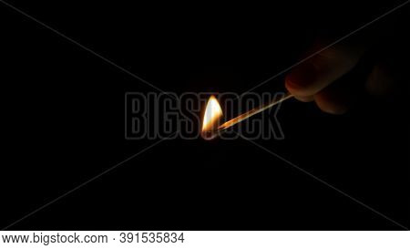 A Human Hand Holds A Burning Match In The Dark. Bright Warm Flame In The Night.