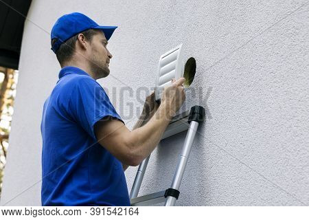 Home Ventilation - Hvac Worker Standing On Ladder And Installing Air Duct Grille On House Facade