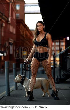 Sexy And Srong Brunette Woman Posing With Bully Dog On City Street, Looking At Camera.