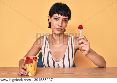 Beautiful brunettte woman eating fresh and healthy fruit relaxed with serious expression on face. simple and natural looking at the camera. 