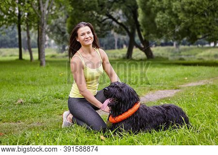 Black Briard Lies On Grass In Park At Summer.