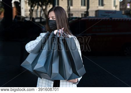 Young Woman With Black Shopping Bags And Medical Mask On Her Face. Black Friday Concep