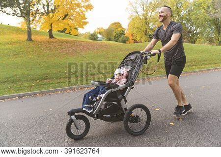 Man With Her Daughter In Jogging Stroller Outside In Autumn Nature