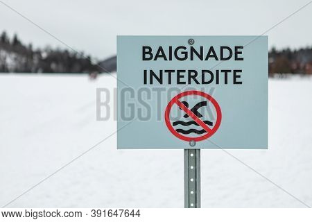 Board On Pole With Text Of Baignade Interdite Written In French Depicting No Swimming With Pictogram