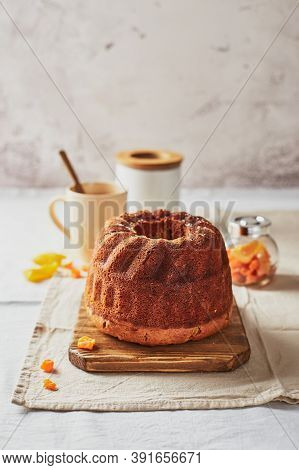Homemade Autumn Carrot Cake With Candied Fruits On Wooden Cutting Board And Cup Of Tea On Light Back