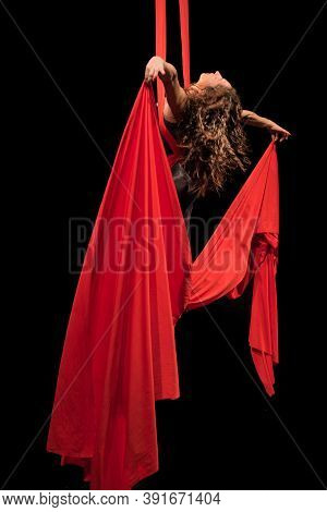 Young woman does aerial acrobatics with red fabrics