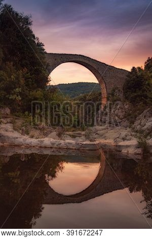 Stone Bridge Reflected On The Water Of A River At Sunset