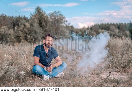 Stylish Bearded Smoker Blows Up A Couple An Electronic Smoke Device In The Calm Outdoors. Vaping.