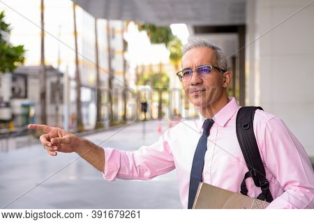 Handsome Persian Businessman With Backpack Hailing Cab Outside Modern Building