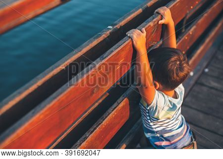 Upper View Photo Of A Caucasian Boy Posing On A Bridge While Looking At The Lake