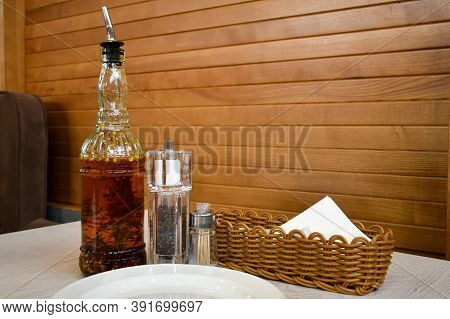 On The Table Are A Glass Bottle Filled With Spicy Olive Oil With Chili And Rosemary And A Salt And P