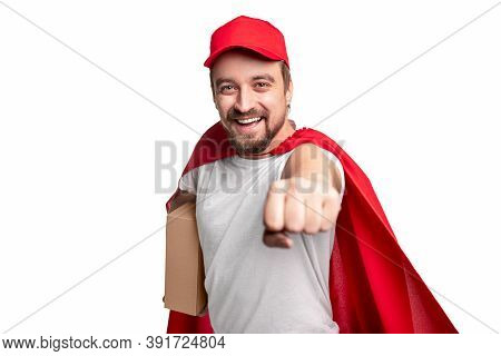 Happy Bearded Courier In Cap And Superhero Cape Carrying Carton Box And Flying To Camera With Clench