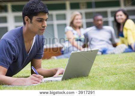 Studente all'aperto sul prato utilizzando Laptop con altri studenti In Background (messa a fuoco selettiva)