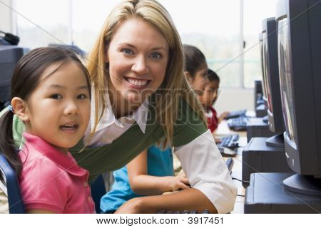 Insegnante aiutare studenti al Computer Terminal con gli studenti In Background (profondità di campo/High Key)