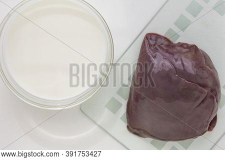 Top View Of Raw Piece Of Liver On Glass Cutboard And Milk In Bowl On The White Background