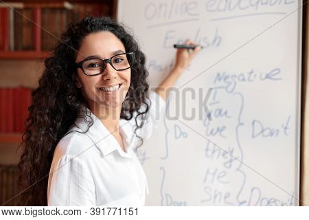 Education And Learning Concept. Portrait Of Smiling Female Teacher Standing At Whiteboard, Explainin