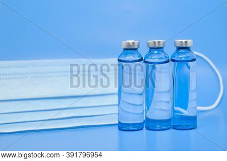 Transparent Medical Ampoules And A Protective Medical Mask On A Light Blue Background. Concept: Medi