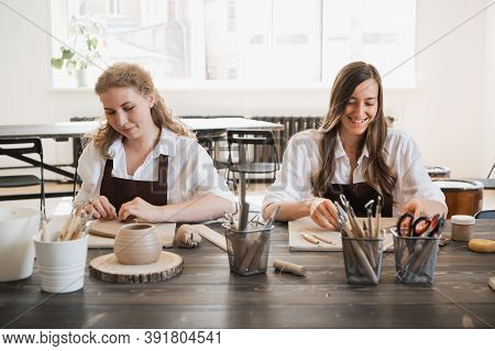 Female Potters Making Clay Pottery At The Table With A Different Wooden Tools. Smiling And Talking A