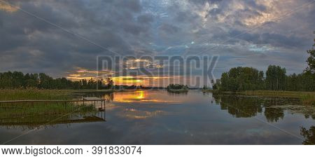 orange sunset in large clowds above river