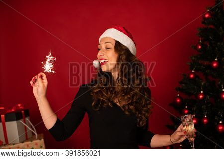 Beautiful Long-hair Brunette Girl In Santa Claus Hat Dancing With Burning Sparklers And Flute Of Cha