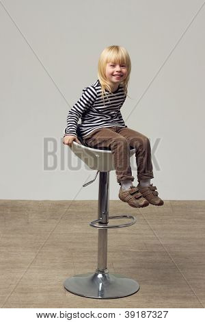 สาวบลอนด์ 3 ปีในกางเกงยีนส์อยู่บนเก้าอี้สูง