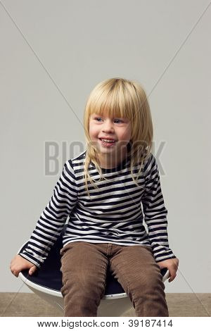 สาวบลอนด์ 3 ปีในกางเกงยีนส์อยู่บนเก้าอี้สูง