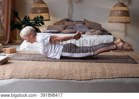 Senior Woman Practicing Yoga At Home Indoor, Doing Salabhasana Or Locust Pose.
