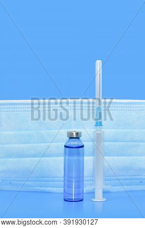 Transparent Medical Ampoules, Syringe And Protective Mask On A Light Blue Background. Concept: Medic