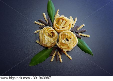 Tagliatelle Pasta, Brown Penne Rigate Pasta, Gemelli Pasta  And Laurel Leaves On A Gray Background.