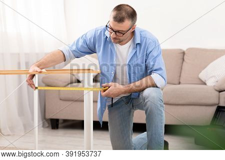 Middle-aged Man Assembling Shelf Using Measuring Tape Furnishing Living Room At Home. Self-assembly 
