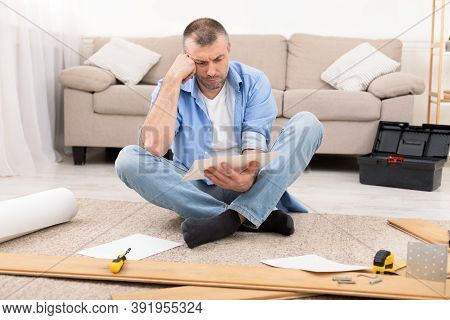 Unhappy Man Reading Furniture Assembly Manual Instruction Installing Cabinet Using Self-assembly Kit