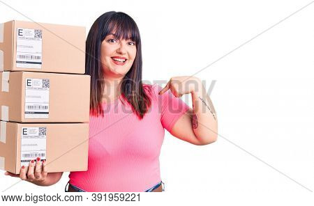Young plus size woman holding delivery package pointing finger to one self smiling happy and proud 