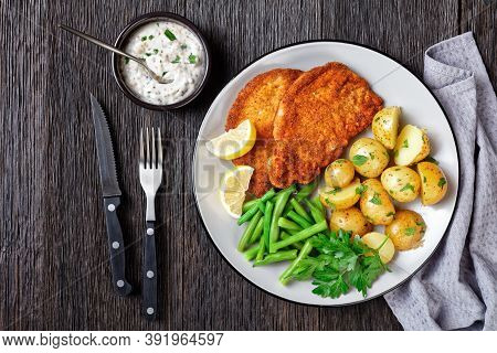 German Pork Schnitzel With Young Potatoes, Green Beans With Cutlery Served On A Plate With Lemon Wed