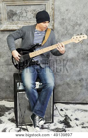 Jeune homme joue de la guitare assis sur l'amplificateur en salle saupoudré de neige