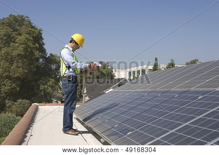 Vista lateral de comprimento total de trabalhador jovem manutenção inspecionar painéis solares no telhado
