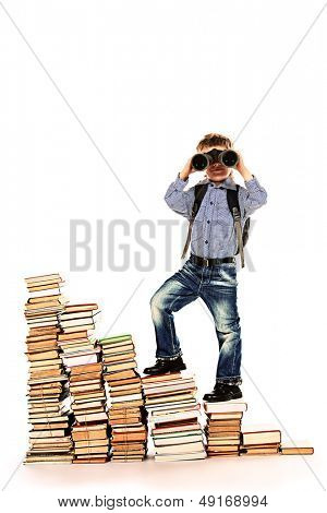 A boy climbing the stairs of books and looking into the distance through binoculars. Isolated over white.