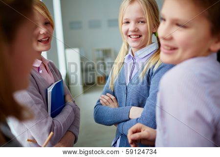 Portrait of three happy schoolgirls and schoolboy talking during school break