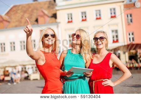 holidays and tourism concept - beautiful blonde girls toursits looking into tablet pc in the city