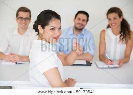 Portrait of happy female candidate gesturing thumbs up with interviewers in background