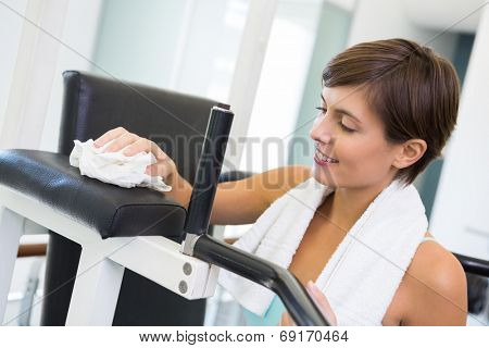 Fit brunette wiping down bench at the gym