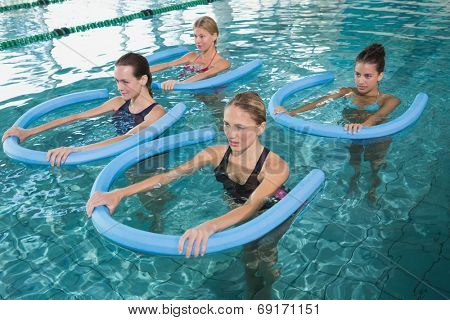 Fitness class doing aqua aerobics with foam rollers in swimming pool at the leisure centre