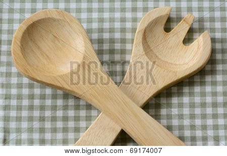 Crossed natural wooden salad fork and spoon on green checkered pattern fabric