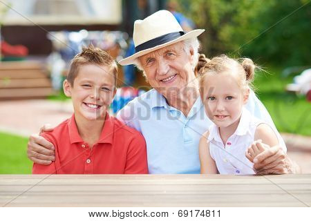 Cute siblings with their grandfather looking at camera at weekend outdoors