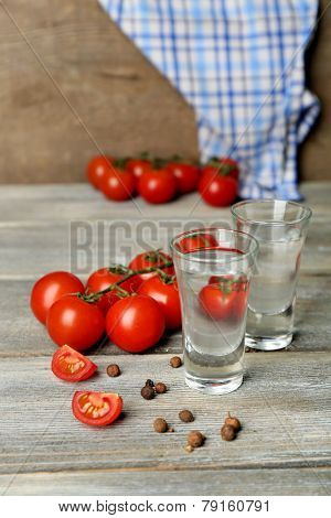 Glasses of ouzo and tomatoes on wooden table